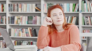 Genç bir kız öğrenci, düşünceli bir şekilde üniversite kütüphanesinde çalışıyor.