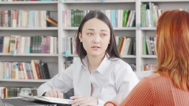 Asiática joven mujer hablando con su amigo en la universidad biblioteca — Vídeos de Stock