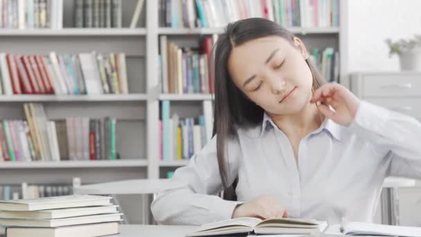 Ung attraktiv kvinnlig student sträcker ryggen medan hon studerar på biblioteket — Stockvideo