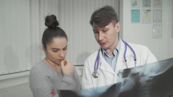 Doctor explicando los resultados del escaneo de rayos X a su paciente femenino — Vídeos de Stock