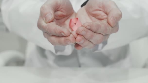 Göğüs kanseri farkındalığı. Bir doktorun elinde pembe kurdele. — Stok video