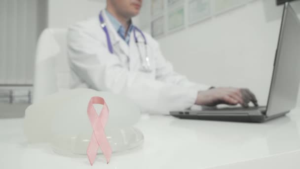 Розовая лента и силиконовые грудные имплантаты на столе врачей — стоковое видео