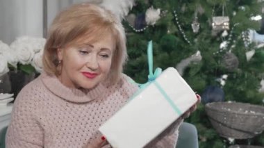 Elinde Noel hediyesiyle kameraya gülümseyen son sınıf öğrencisi kadın.