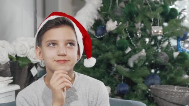 戴着圣诞老人帽子的可爱的小男孩若有所思地把目光移开 — 图库视频影像