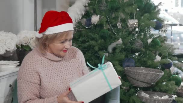 Szczęśliwy starszy kobieta w Santa Claus kapelusz gospodarstwa prezent świąteczny — Wideo stockowe
