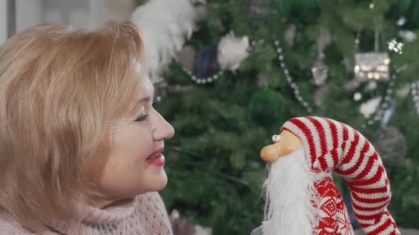 Wesoła starsza kobieta śmieje się do kamery trzymając zabawną zabawkę Santa Claus — Wideo stockowe