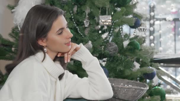 Herrliche Frau lächelt in die Kamera, wenn sie zu Hause am Weihnachtsbaum sitzt — Stockvideo