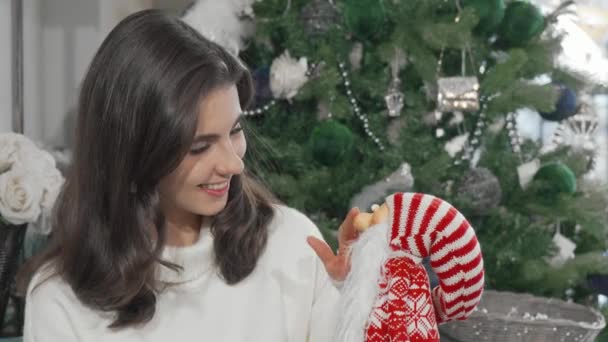 Charmante schöne Frau lächelt in die Kamera und hält niedliches Weihnachtsmann-Spielzeug in der Hand — Stockvideo