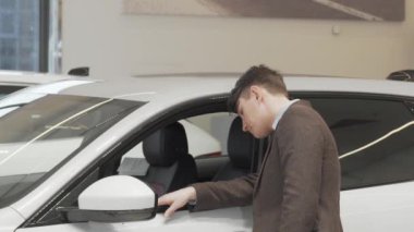 Yetişkin bir adamın galeride satışta olan yeni bir arabanın içine baktığı arka plan fotoğrafı.