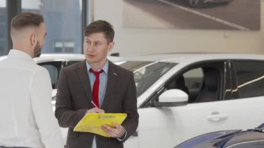 Olgun satıcı, erkek müşterinin otomobil almasına yardım ediyor.