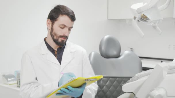 Dentista profissional preenchendo documentos médicos em seu escritório — Vídeo de Stock