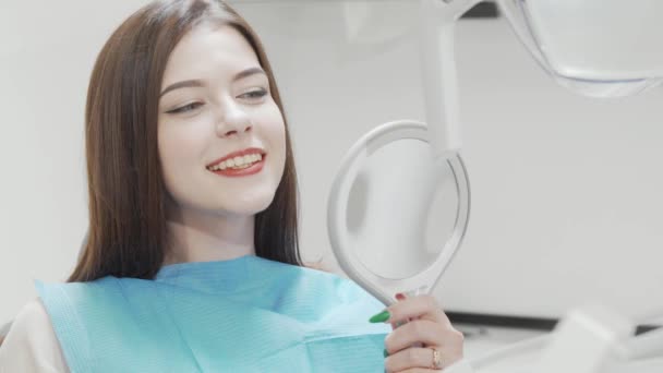 美しい女性は彼女の歯を鏡の中の歯科医院で調べる — ストック動画