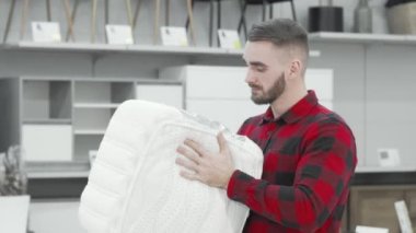 Mobilya mağazasında ortopedik yatak örneklerini inceleyen yakışıklı bir adam.