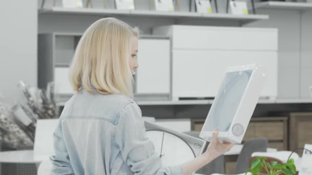 Cliente femenino eligiendo entre dos relojes de pared en la tienda de muebles — Vídeos de Stock