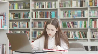 Genç kız öğrenci kütüphanede bir proje üzerinde çalışırken strese giriyor.