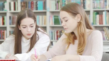 Liseli kız arkadaşlar kütüphanede birlikte okuyorlar.