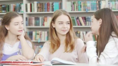 Okul kütüphanesinde sohbet eden üç genç kız arkadaş.