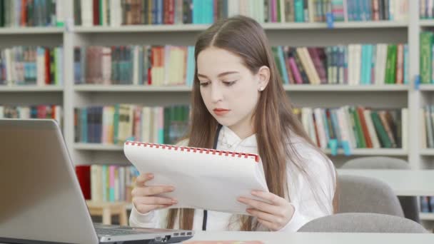 Charmig tonårstjej som läser lärobok på biblioteket — Stockvideo