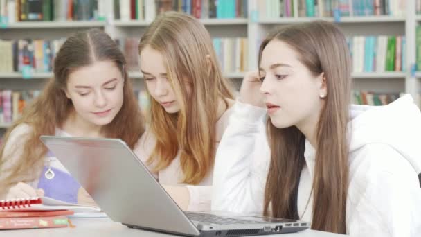 Adolescente usando seu laptop enquanto estudava na biblioteca com amigos — Vídeo de Stock