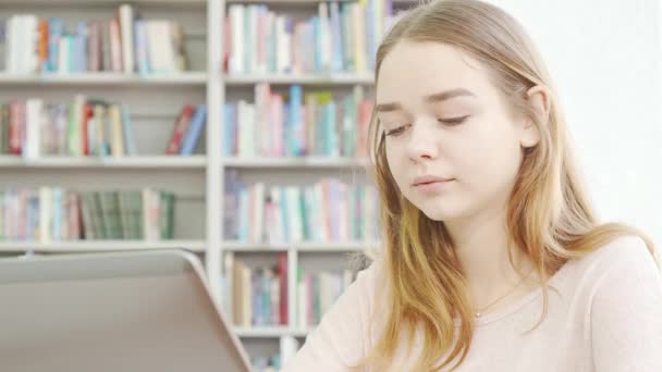 Kedves tini lány használja laptop a könyvtárban — Stock videók
