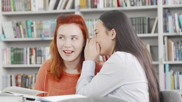 Amigas universitarias susurrando y riendo en la biblioteca —  Fotos de Stock