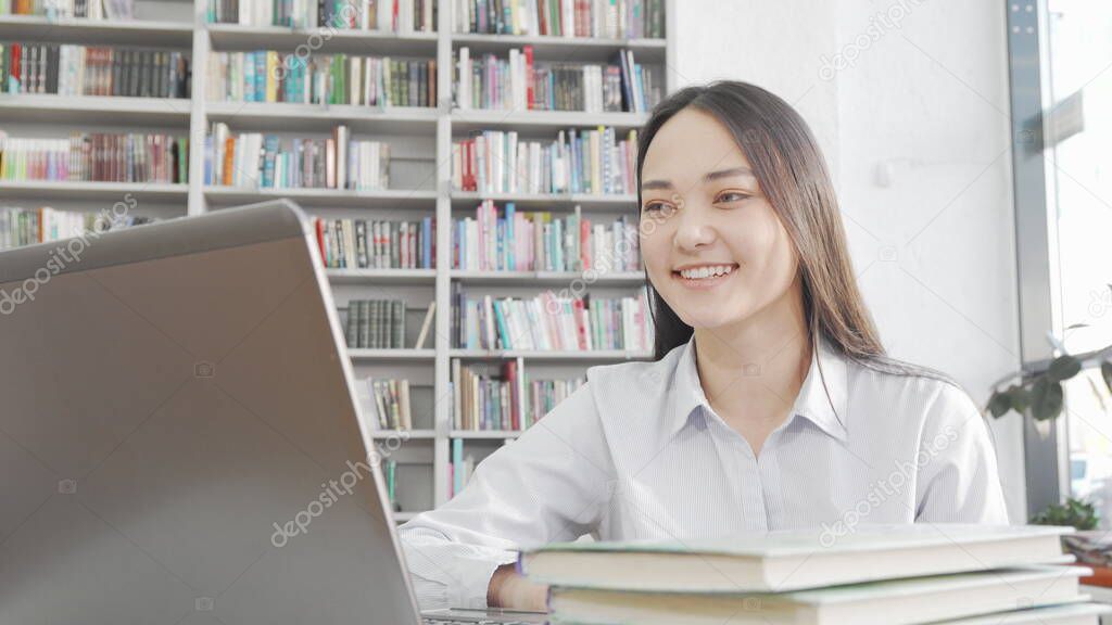 Charming Asian woman laughing while using laptop at the library
