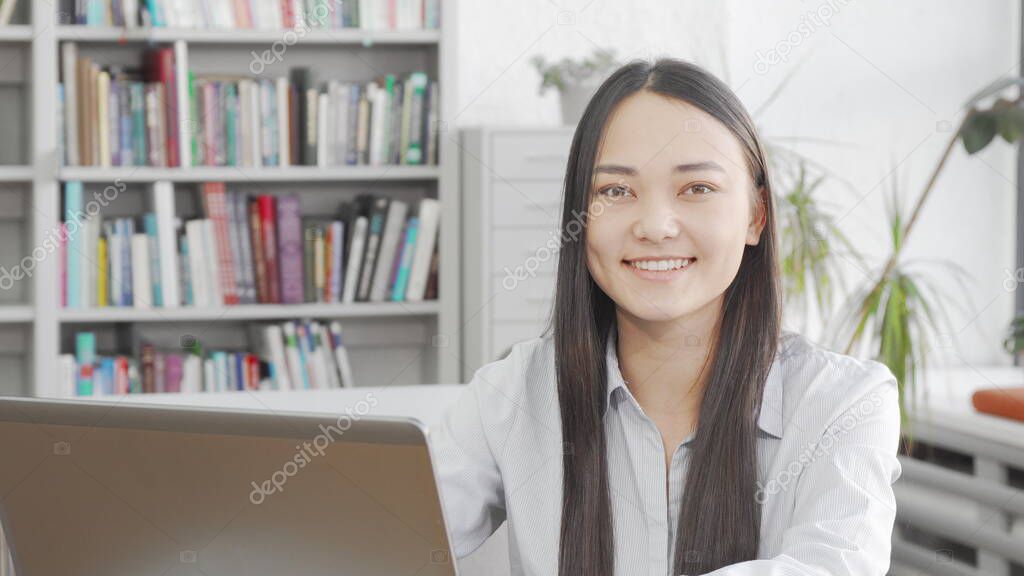 Asian young woman smiling to the camera while using laptop at library