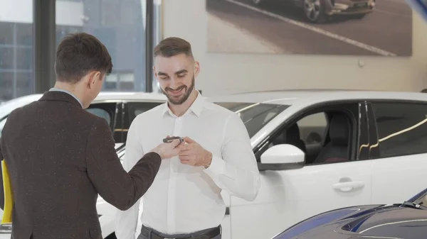 Jovem feliz recebendo chaves de carro para o seu novo automóvel do vendedor — Fotografia de Stock