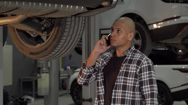 Jovem africano falando ao telefone na estação de reparo do carro Imagem De Stock