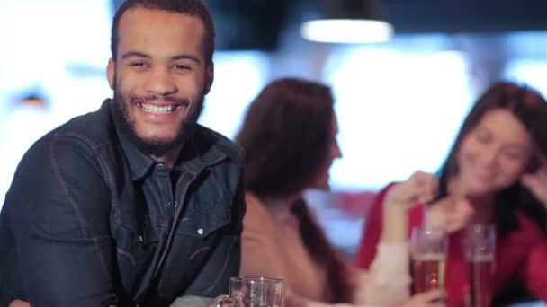 Lächelnder afrikanischer Mann auf dem Hintergrund zweier Mädchen in einer Bar — Stockvideo