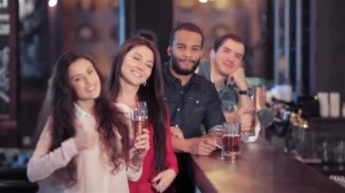 Bir grup arkadaşıyla birlikte gülümseyen ve başparmak göstermek yukarıya bir bira ile bir bar