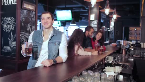 Парень со стаканом пива в баре смотрит футбол на фоне своих друзей — стоковое видео