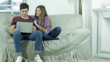 Kanepede oturan erkek arkadaşının omuzlarına sarılan kız