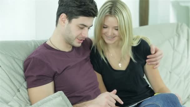 Lustiges Paar, das auf einer Couch in einer Umarmung mit dem Tablet sitzt — Stockvideo