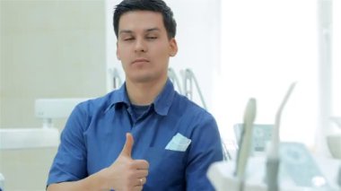 Gülümseyen ve başparmak kameraya gösteren diş hekimi