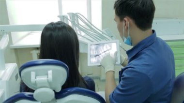 Diş hekimi bir hastanın röntgeni dişlerini tablet üzerinde gösterir.