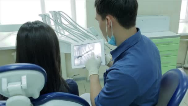 Дантист показывает пациентке рентген на таблетке зубов и рассказывает о методе лечения каналов — стоковое видео
