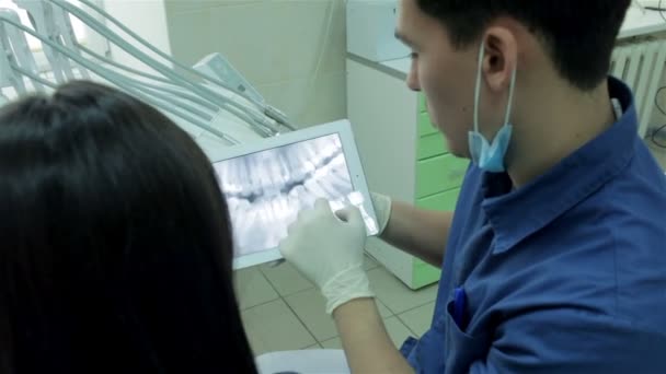Dentysta pokazuje RTG pacjenta na tablecie i opowiada jej metoda korekcji ukąszenie ząb — Wideo stockowe