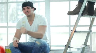 Bir pencere üzerinde oturan işçi ressam gülümseyerek