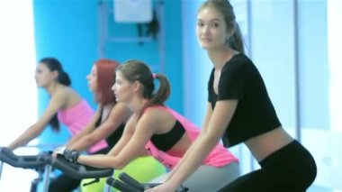 Pedal ve sabit bir bisiklet üzerinde kameraya bakarak atletik kız