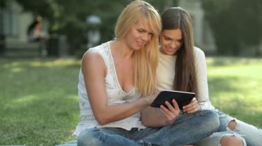 Bir tablet kullanarak çim üzerinde oturan