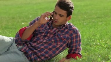 Cep telefonu kullanarak çimenlerin üzerinde yatan adam