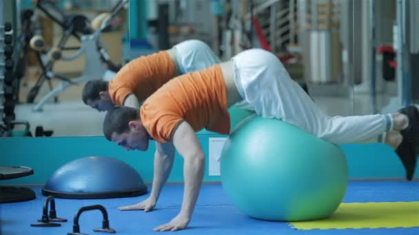 Hombre joven con una camisa roja haciendo ejercicio en fit-ball — Vídeo de stock