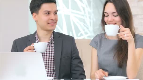 Молодий привабливий бізнесмен і жінка п'ють каву і посміхаються для обговорення даних, що зіштовхуються — стокове відео