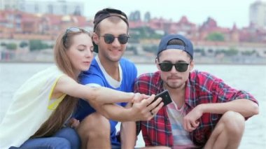 Üç arkadaş oturup nehre gülüyorve birbirlerinin resimleri