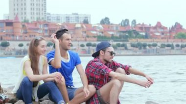 Üç arkadaş oturup gülüyor ve nehre taş atıyorlar.