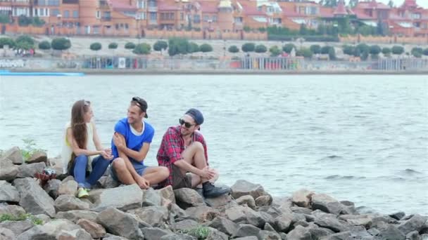 Tres amigos sentados y riendo en las rocas junto al río — Vídeos de Stock