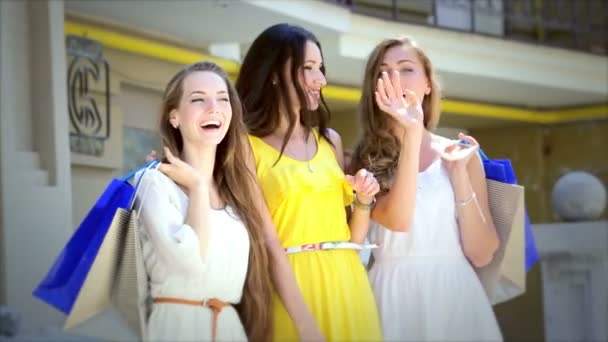 Три девушки стоят с сумками для покупок и машут друзьями. — стоковое видео