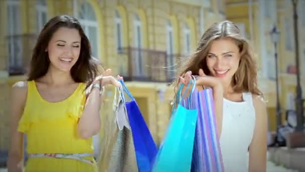 Dos chicas jóvenes glamorosas van de la mano con bolsas de compras — Vídeos de Stock