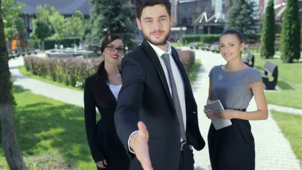 Успешный бизнесмен пожимает руку, стоя в компании двух женщин — стоковое видео